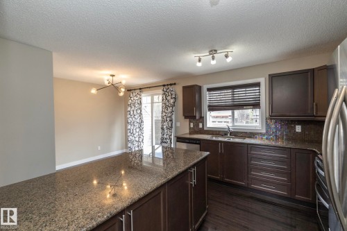 Kitchen featuring an expansive island with a granite countertop, dark wood-finish cabinetry, stainless steel appliances, a mosaic tile backsplash, and dark wood-finish flooring - 117 Callaghan Drive Sw, Edmonton, AB - Indoor Photo Showing Kitchen With Double Sink