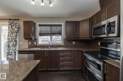 Contemporary kitchen featuring dark wood cabinetry, granite-finish countertops, stainless steel appliances, a mosaic tile backsplash, and dark wood-finish flooring - 