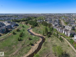 Expansive green space featuring a winding creek, mature trees, and paved pedestrian paths - 