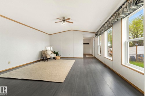 Spacious living area featuring wood-finish flooring, white panel walls with wood trim, multiple large windows, and a ceiling fan with integrated lighting - 49 Rim Road Nw, Edmonton, AB - Indoor Photo Showing Other Room