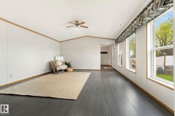 Spacious living area featuring wood-finish flooring, white panel walls with wood trim, multiple large windows, and a ceiling fan with integrated lighting - 