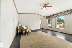 Spacious room featuring dark wood-finish flooring, white panel walls with wood trim, and a ceiling fan with integrated lighting - 