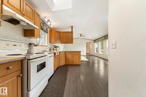 Kitchen featuring wood cabinetry, white appliances, a skylight, and wood-finish flooring extending into an open living area with multiple windows - 49 Rim Road Nw, Edmonton, AB - Indoor Photo Showing Kitchen