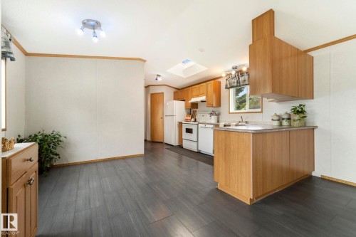 Open-concept kitchen and dining area featuring wood-finish flooring, wood cabinetry, a skylight, and white appliances - 49 Rim Road Nw, Edmonton, AB - Indoor Photo Showing Kitchen