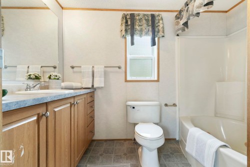 Bathroom featuring a light wood-finish vanity with a single basin sink, a large wall-mounted mirror, a standard toilet, and a combined shower and bathtub unit - 49 Rim Road Nw, Edmonton, AB - Indoor Photo Showing Bathroom