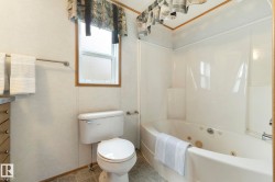 Bathroom featuring a white jetted tub, a white toilet, a window with wood trim, and a vanity with a countertop - 