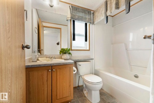 Bathroom featuring a light wood vanity with a single basin sink, a gray countertop, a full-size mirror, and a white tub with shower surround - 49 Rim Road Nw, Edmonton, AB - Indoor Photo Showing Bathroom