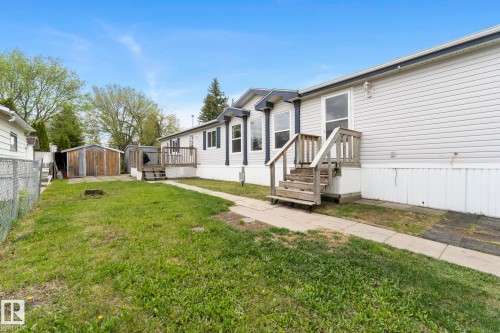 Side elevation of the property featuring a light-colored siding exterior, multiple windows, and a wooden deck with stairs - 49 Rim Road Nw, Edmonton, AB - Outdoor
