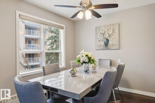 Dining area featuring a modern dining table with four chairs, a ceiling fan with integrated lighting, and a large window providing natural light - 202 17511 98A Avenue, Edmonton, AB - Indoor Photo Showing Dining Room