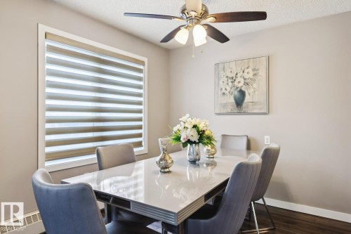 The dining area features a large window with horizontal blinds, a ceiling fan with integrated lighting, and dark wood flooring - 202 17511 98A Avenue, Edmonton, AB - Indoor Photo Showing Dining Room