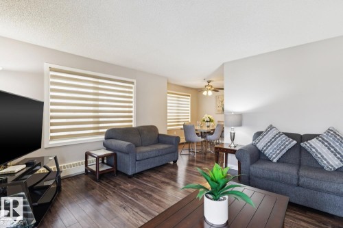 Living area featuring dark wood floors, large windows with blinds, and light grey walls - 202 17511 98A Avenue, Edmonton, AB - Indoor Photo Showing Living Room