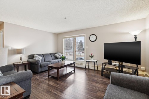 Living area featuring hard surface flooring, light-colored walls, and a sliding glass door leading to an outdoor space - 202 17511 98A Avenue, Edmonton, AB - Indoor Photo Showing Living Room
