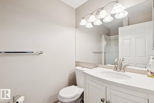 Bathroom featuring a white vanity with an integrated sink, a large mirror, and a modern light fixture with multiple frosted glass shades - 202 17511 98A Avenue, Edmonton, AB - Indoor Photo Showing Bathroom