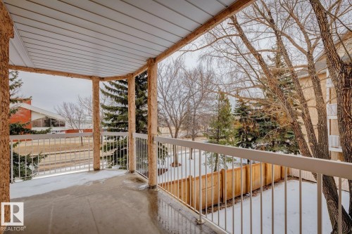 The property features a private balcony with a concrete floor and a white metal railing, offering views of the surrounding area with trees and a wooden fence - 202 17511 98A Avenue, Edmonton, AB - Outdoor With Balcony