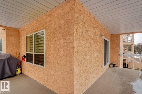 The property features a concrete patio with a textured exterior wall, white-framed windows, and a white slatted ceiling - 202 17511 98A Avenue, Edmonton, AB - Outdoor With Exterior