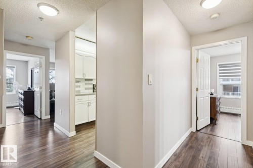The property features cohesive dark wood flooring throughout the hallway and into the visible rooms - 202 17511 98A Avenue, Edmonton, AB - Indoor Photo Showing Other Room