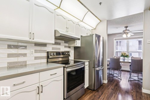 The kitchen features white cabinetry, stainless steel appliances, a tile backsplash, and dark wood flooring - 202 17511 98A Avenue, Edmonton, AB - Indoor Photo Showing Kitchen With Stainless Steel Kitchen