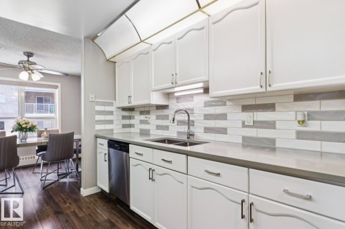The kitchen features white cabinetry, a light-colored countertop, and a tiled backsplash with a mix of white and grey rectangular tiles - 202 17511 98A Avenue, Edmonton, AB - Indoor Photo Showing Kitchen With Double Sink