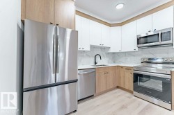 Modern kitchen featuring stainless steel appliances, two-tone cabinetry, marble-patterned backsplash, light wood-finish flooring, and recessed ceiling lighting - 