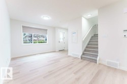 Bright entry area featuring wood-finish flooring, a carpeted staircase with a white handrail, recessed lighting, and a front door with a windowpane - 