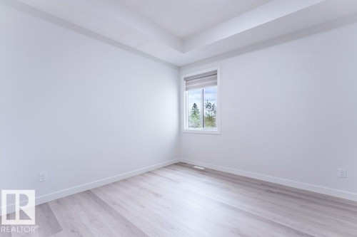 Bright room featuring a single window with roller shade, wood-finish flooring, white baseboards, and a tray ceiling - 6920/6922 106 Street, Edmonton, AB - Indoor Photo Showing Other Room