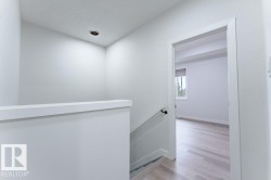 Upper-level hallway featuring a recessed ceiling light, white painted walls, and a staircase with a black handrail - 