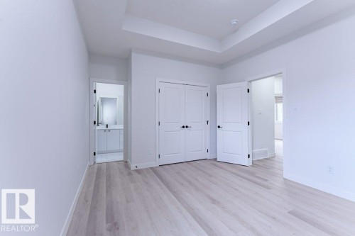 Spacious room featuring light wood-finish flooring, a tray ceiling, and white panel doors with black hardware - 6920/6922 106 Street, Edmonton, AB - Indoor