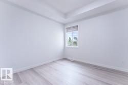 Bright room featuring a single window with roller shade, wood-finish flooring, white baseboards, and a tray ceiling - 