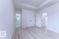 Spacious room featuring light wood-finish flooring, a tray ceiling, and white panel doors with black hardware - 