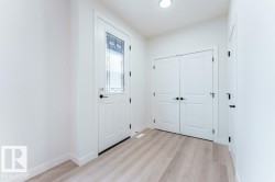 Entryway featuring a white paneled door with decorative glass inserts, matte black hardware, light wood-finish flooring, and a recessed ceiling light - 