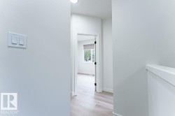 Hallway entry into a room featuring light-toned wood-finish flooring, white walls, and a window with a roller shade - 