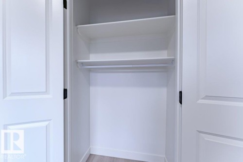 White bi-fold doors reveal a closet interior featuring two upper shelves and a clothing rod - 6920/6922 106 Street, Edmonton, AB - Indoor