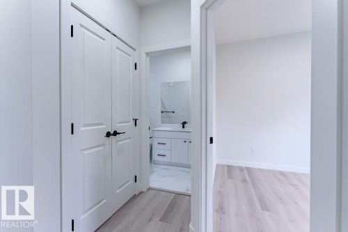 Hallway featuring light wood-finish flooring, white walls, and a built-in closet with bi-fold doors and matte black hardware - 6920/6922 106 Street, Edmonton, AB - Indoor Photo Showing Other Room