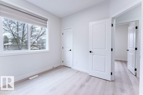 Room featuring wood-finish flooring, white walls, and a large window with a roller shade - 6920/6922 106 Street, Edmonton, AB - Indoor Photo Showing Other Room