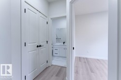 Hallway featuring light wood-finish flooring, white walls, and a built-in closet with bi-fold doors and matte black hardware - 