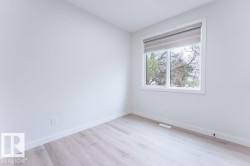 Bright room featuring a large window with roller shades, light wood-finish flooring, white baseboards, and crisp white walls - 