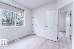 Room featuring wood-finish flooring, white walls, and a large window with a roller shade - 