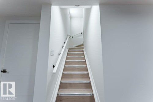 Staircase with wood-finish treads, light-toned risers, and a white wall-mounted handrail with dark brackets - 6920/6922 106 Street, Edmonton, AB - Indoor Photo Showing Other Room