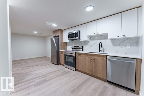 Modern kitchen featuring two-tone cabinetry, stainless steel appliances, a black matte faucet, and light wood-finish flooring - 6920/6922 106 Street, Edmonton, AB - Indoor Photo Showing Kitchen