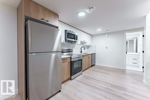 Contemporary kitchen featuring stainless steel appliances, a white marble-look backsplash, light wood-finish and white cabinetry, and wood-finish flooring - 6920/6922 106 Street, Edmonton, AB - Indoor Photo Showing Kitchen