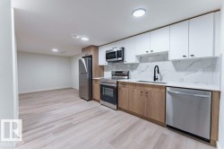 Modern kitchen featuring two-tone cabinetry, stainless steel appliances, a black matte faucet, and light wood-finish flooring - 