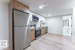 Contemporary kitchen featuring stainless steel appliances, a white marble-look backsplash, light wood-finish and white cabinetry, and wood-finish flooring - 