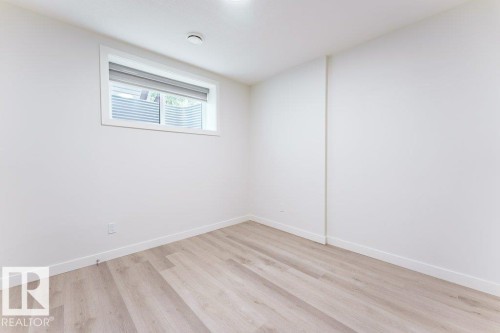 Light-filled room featuring a single window with a window well, light wood-finish flooring, white walls, white baseboards, and a flush-mount ceiling light - 6920/6922 106 Street, Edmonton, AB - Indoor Photo Showing Other Room
