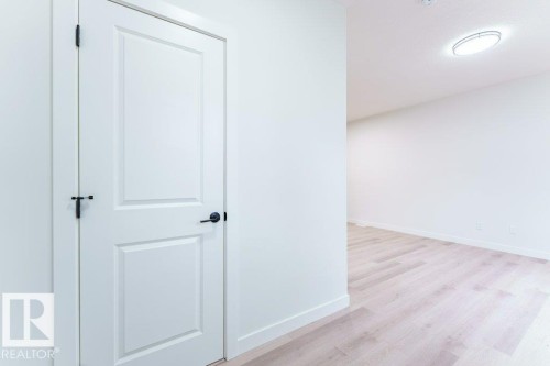 White interior door with black hardware, white baseboards, and wood-finish flooring - 6920/6922 106 Street, Edmonton, AB - Indoor Photo Showing Other Room