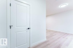White interior door with black hardware, white baseboards, and wood-finish flooring - 