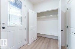 Entryway featuring a white paneled door with decorative glass, black hardware, and wood-finish flooring - 
