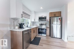 Modern kitchen featuring a window above the sink, stainless steel appliances, two-tone cabinetry, light-toned countertops, and wood-finish flooring - 