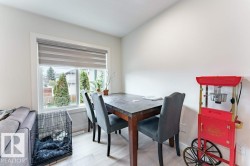 Bright dining area featuring a large window with horizontal blinds, light wood-finish flooring, and crisp white walls - 