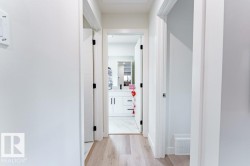 Hallway featuring light wood-finish flooring, white walls, and bright overhead lighting - 