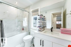 Contemporary bathroom featuring a white bathtub with a glass sliding door, white marble-look tile surround, and a white vanity with a rectangular undermount sink - 